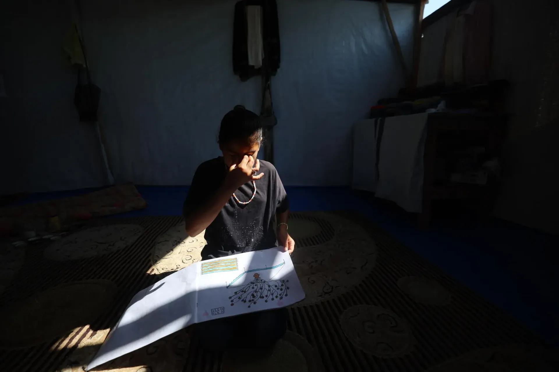 Gaza Strip. A child draws a picture as light casts a shadow on the paper at a Teaching Recovery Techniques session.