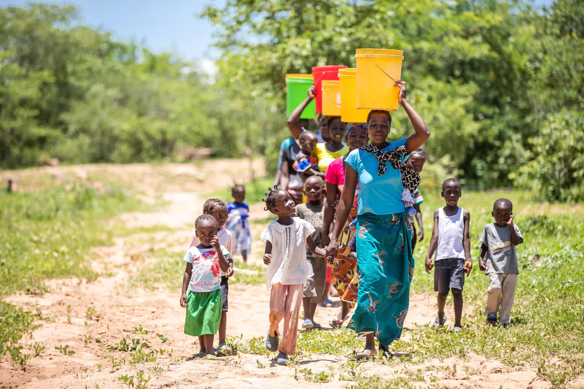 Women carrying buckets over their heads walk along with children to collect water in Zambia.