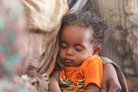 Un enfant dort sur les genoux de sa mère.
