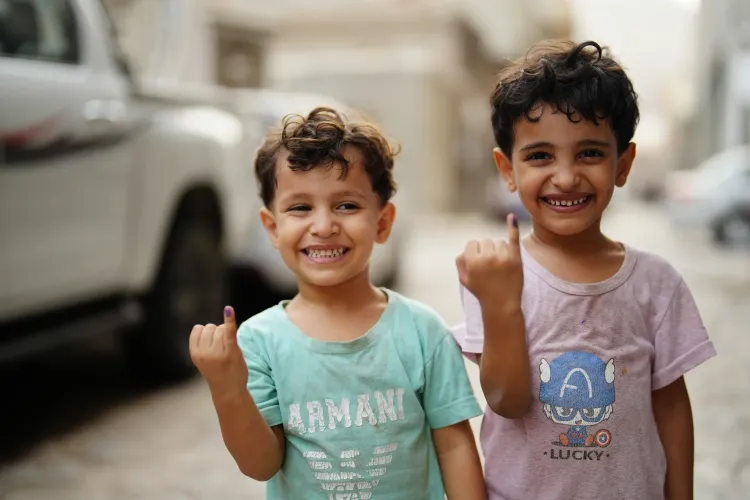 Two boys smile widely while holding up their pinky fingers, marked purple after receiving a polio vaccine.