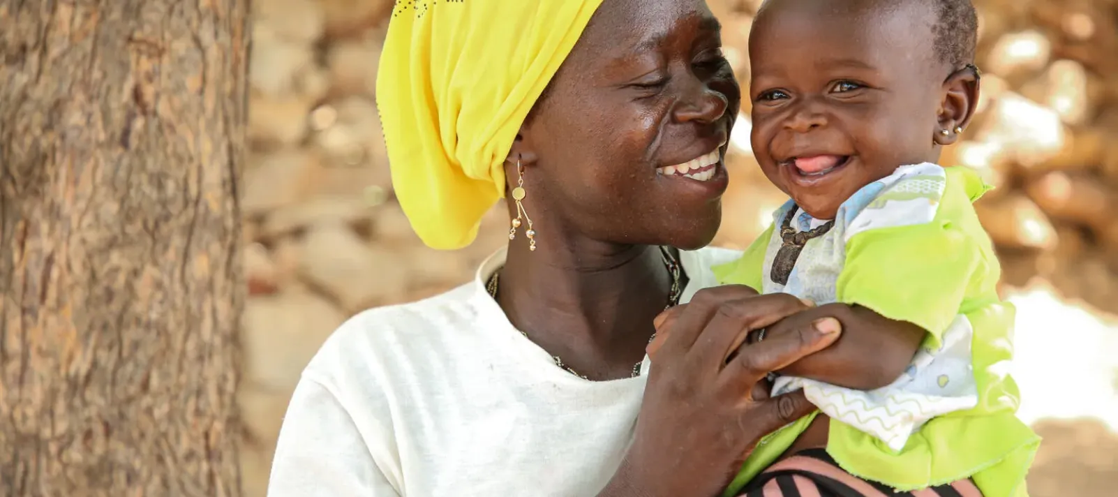 Une mere tient son enfant dans les bras, tous les deux sourient. 