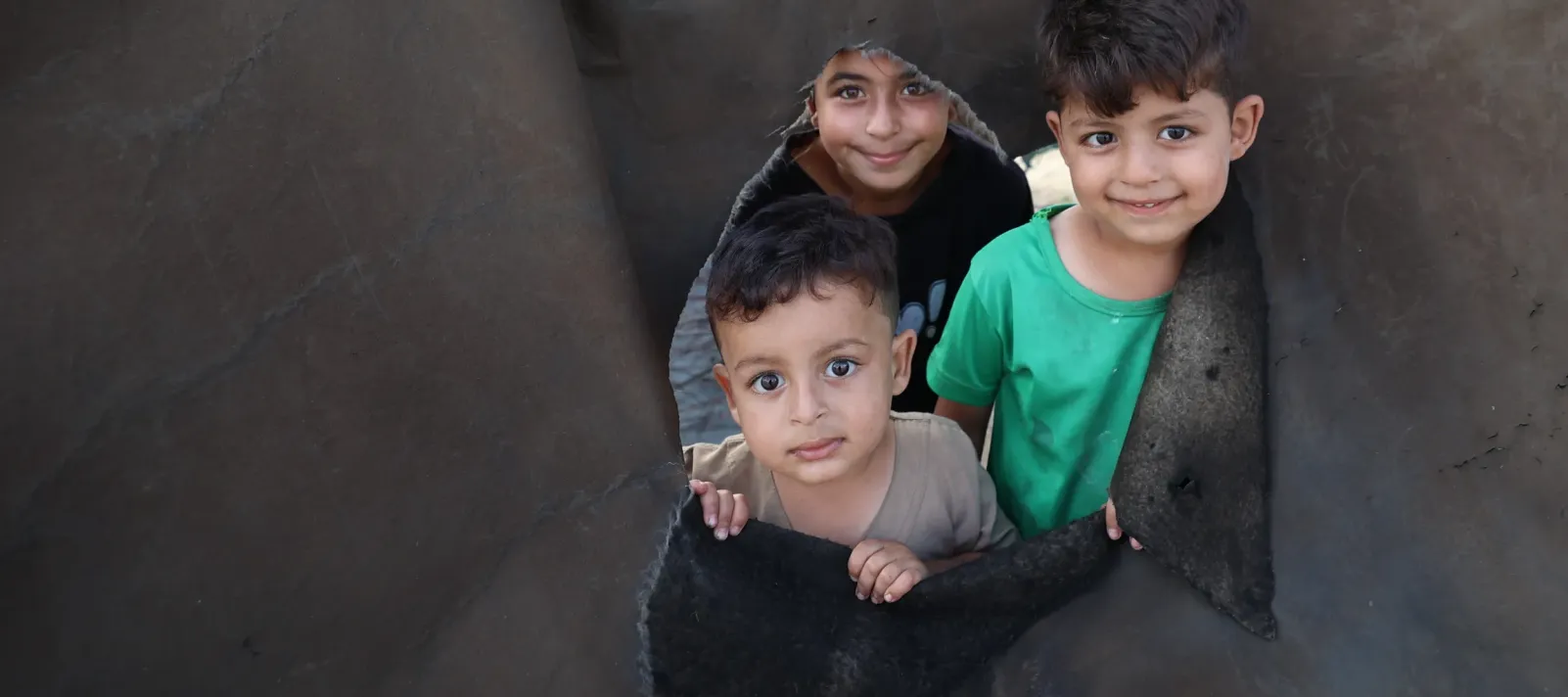 Three children look out from a hole in a tent following the ceasefire announcement in Gaza.