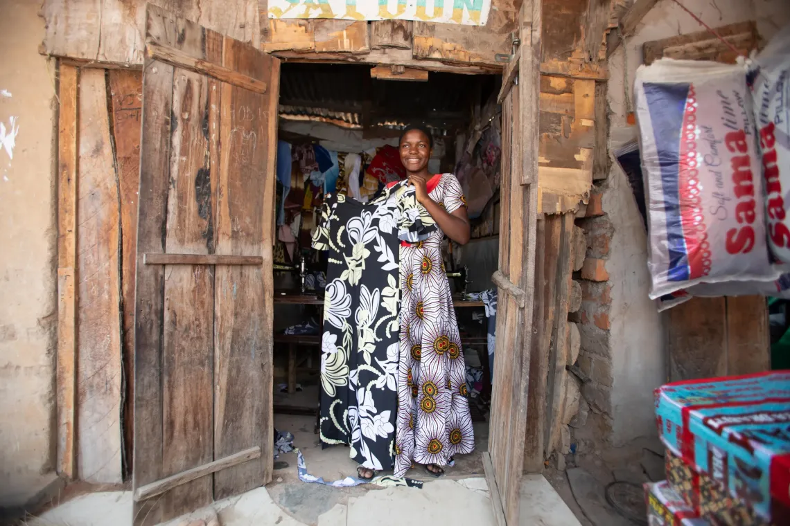 Smiling, Antini holds up a black and white printed dress she has made.