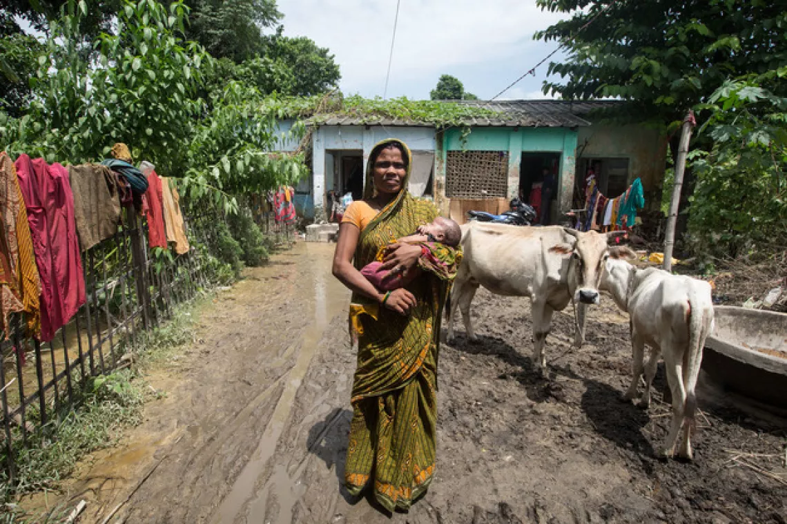 A  mother in Nepal stands infront of her flood affected house holding her baby