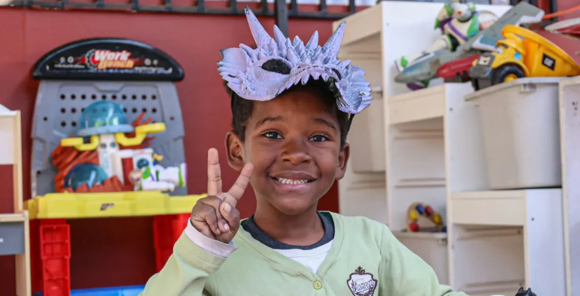 A child smiles while holding the peace sign