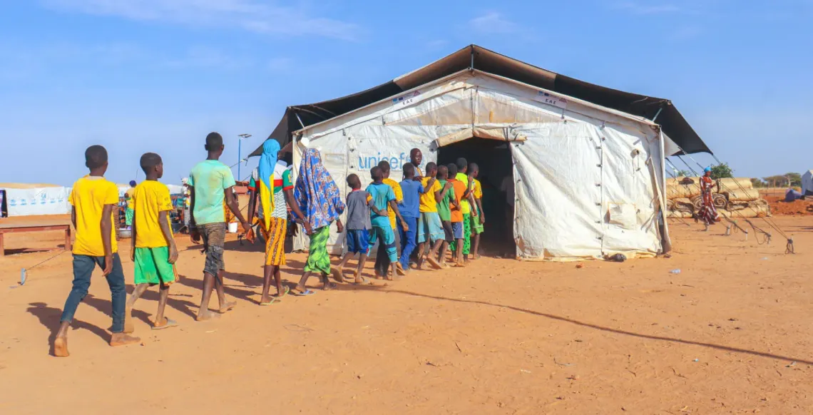 A line of children walking into a large tent