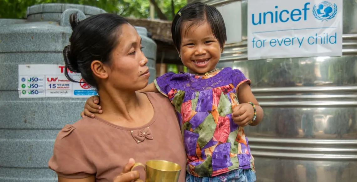 A woman holds a child in one arm and a cup in another