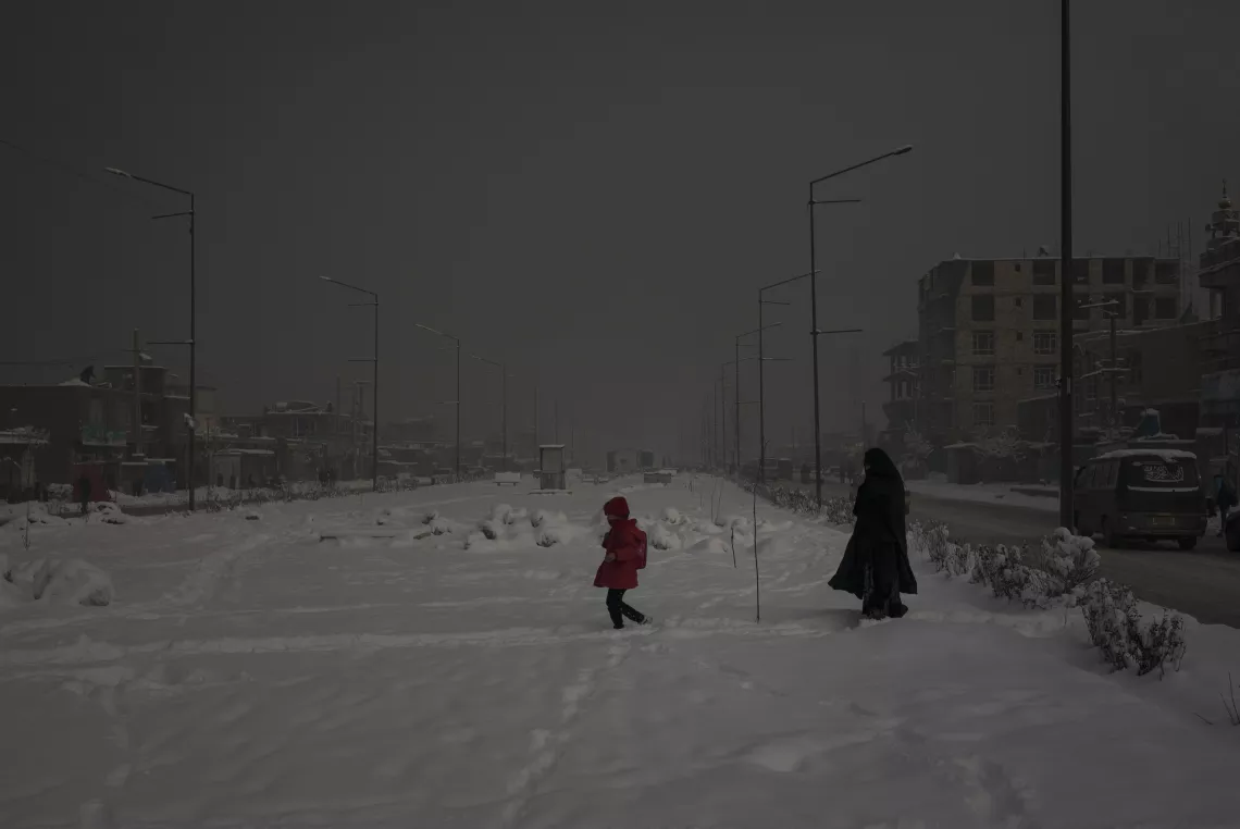 A woman and child walk on snow on a hazy day in Afghanistan