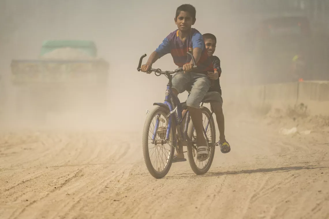 Two boys riding a bicycle on a dusty road