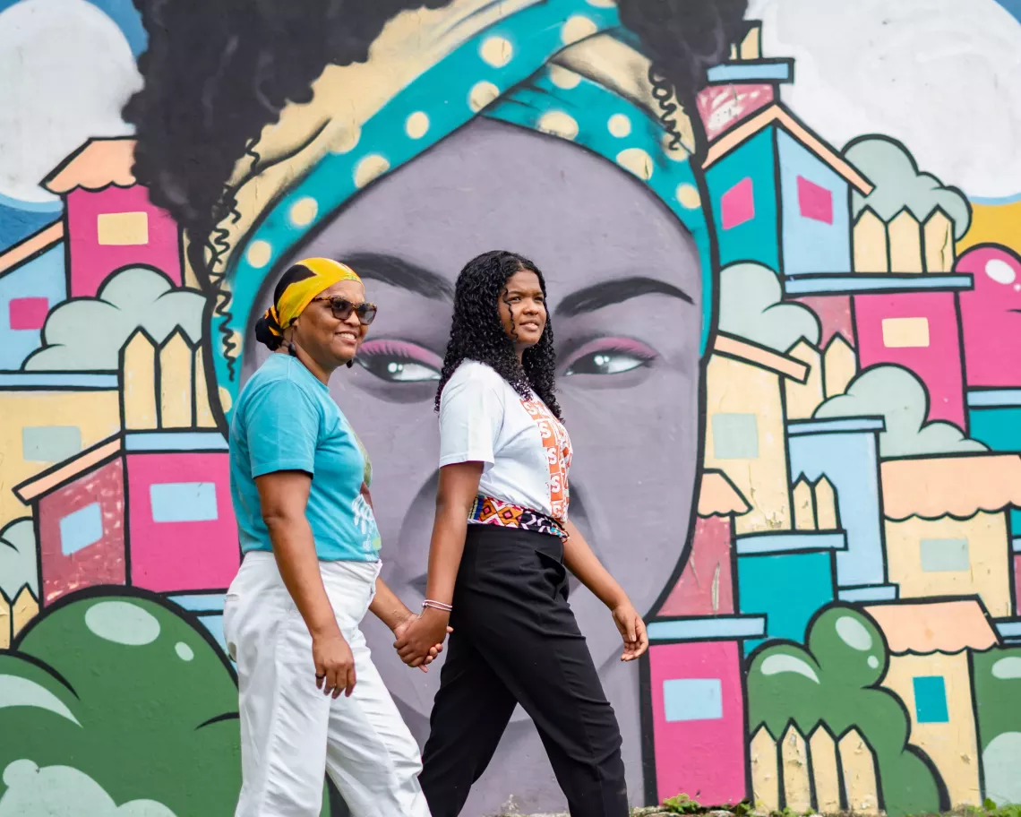 A woman and her daughter walk past a brightly painted mural of woman's face.