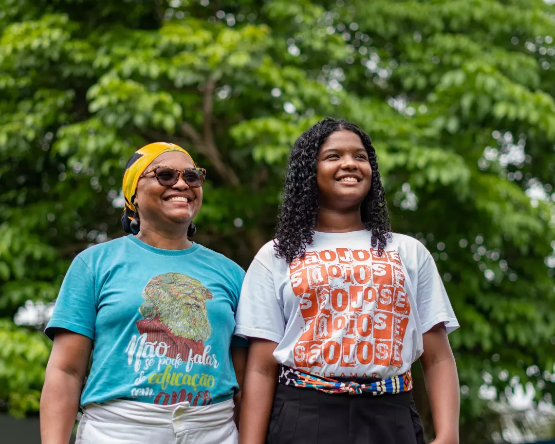 A mother and daughter stand proudly next each other smiling.
