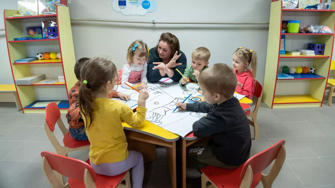 Une enseignante accompagne de jeunes enfants participant &agrave; un atelier de coloriage.