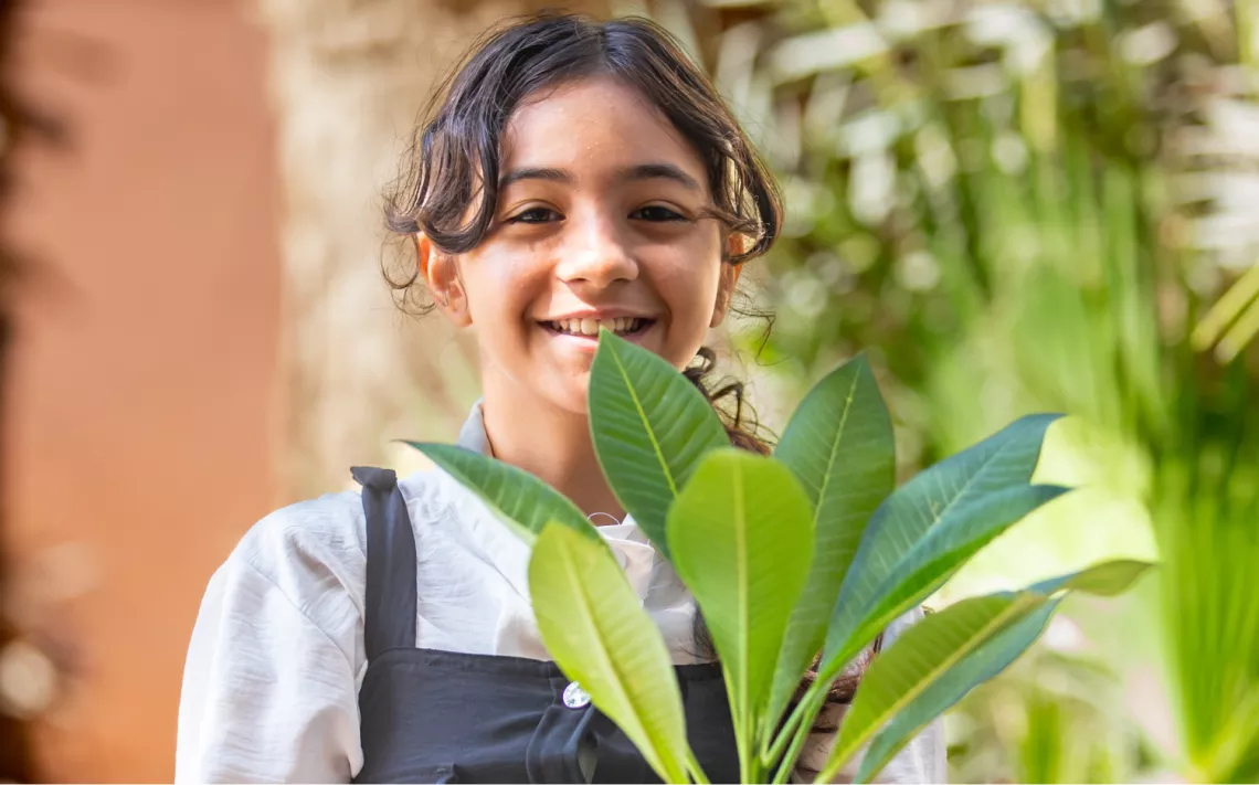 A girl stands behind a green plant