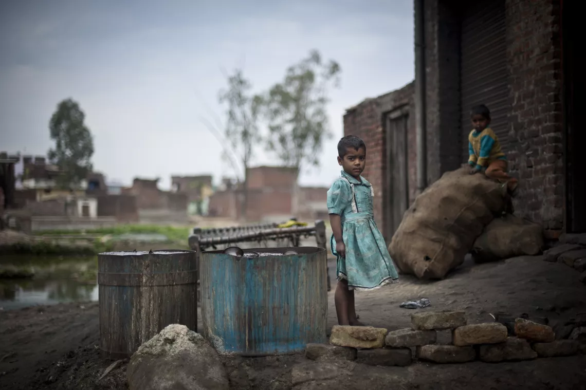 A young girl and boy play outside a metal polishing workshop in a slum in India.