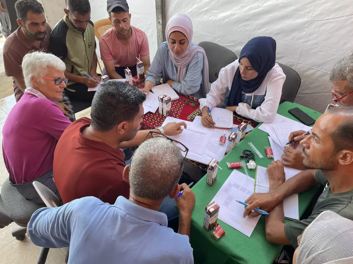 UNICEF staff and the community committee sit together to plan and prepare for children&rsquo;s return to learning in a makeshift shelter.