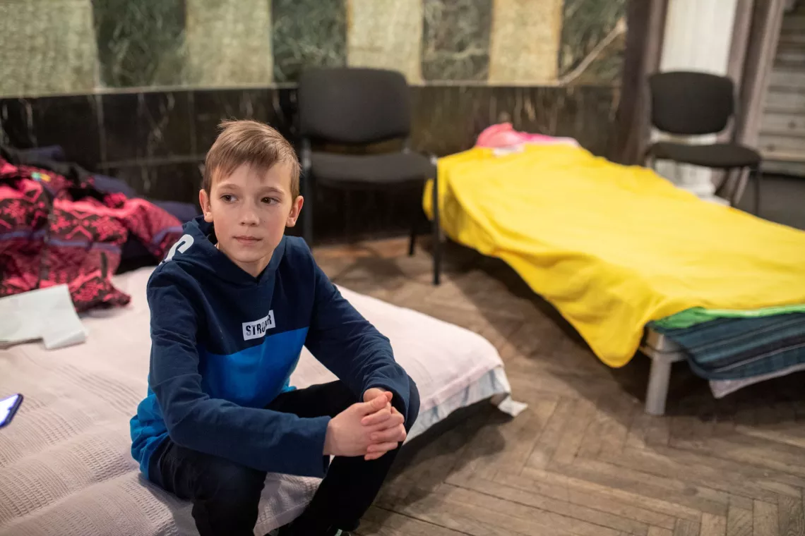 Ukraine. A boy sits on a bed in a temporary shelter at a theatre.