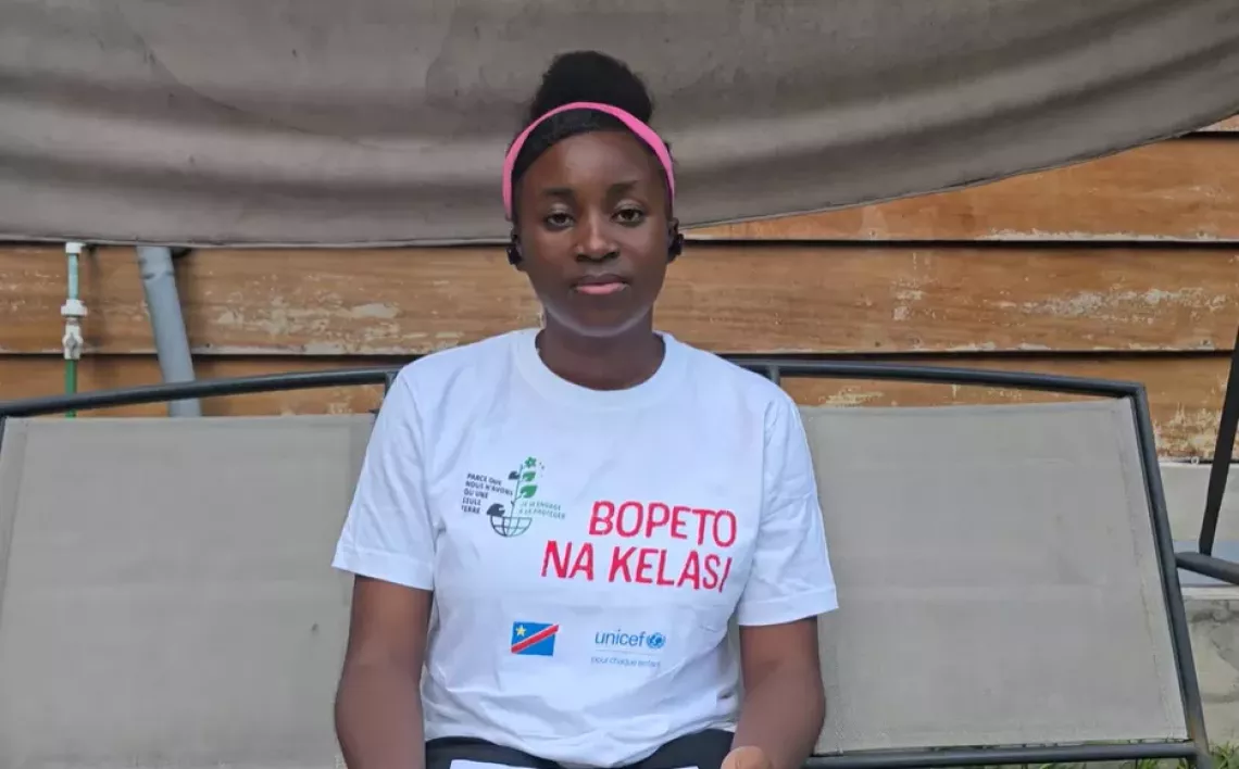 A 15-year-old girl in DRC sits on an outdoor bench.