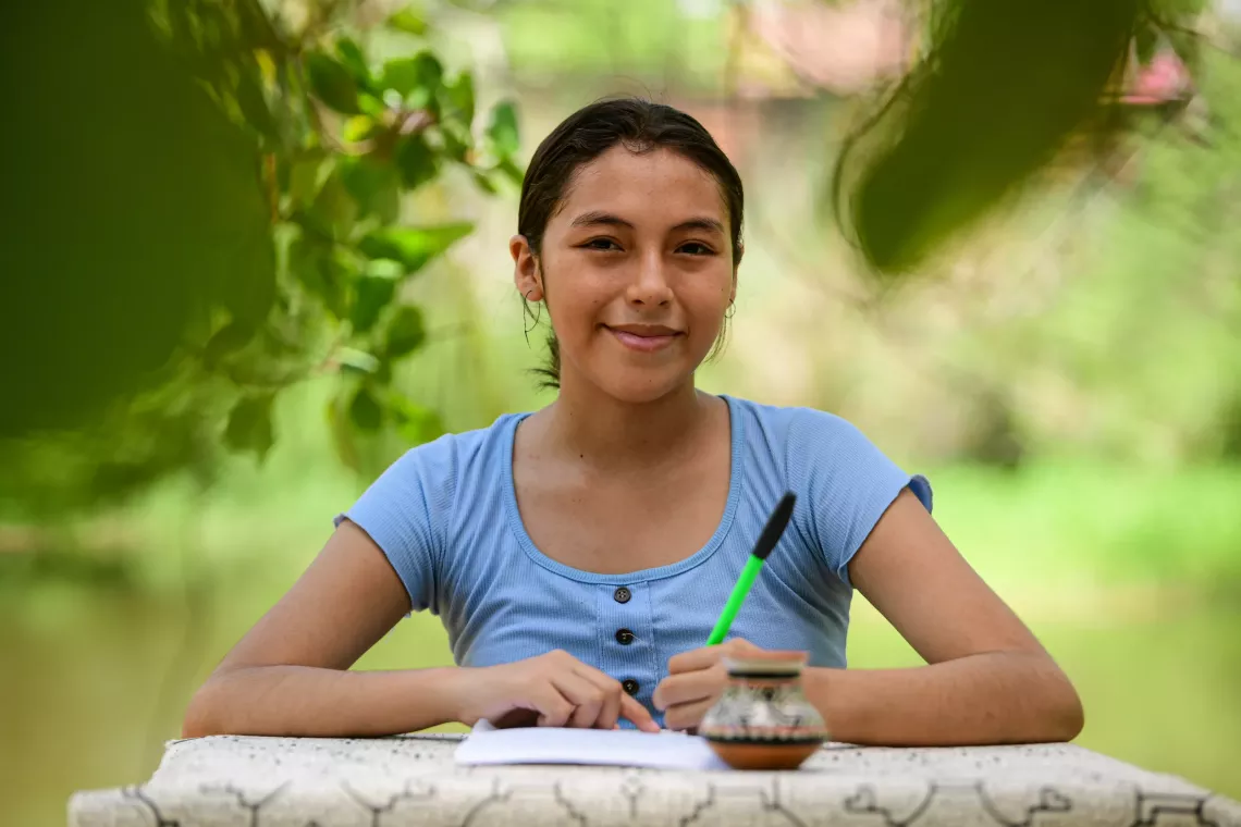 A girl sits at an outdoor table writing a letter.