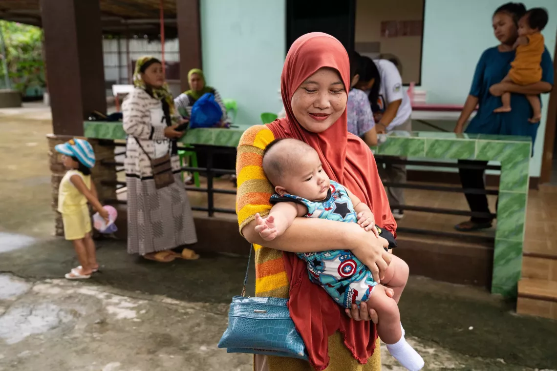 A smiling mother leaving a health center carrying her infant child 