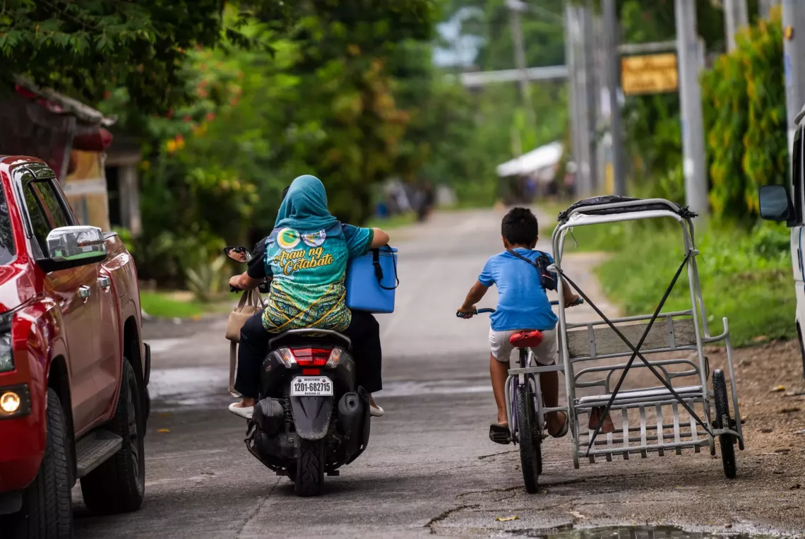 A healthcare worker rides on the back of a motorbike holding with a vaccine carrier 