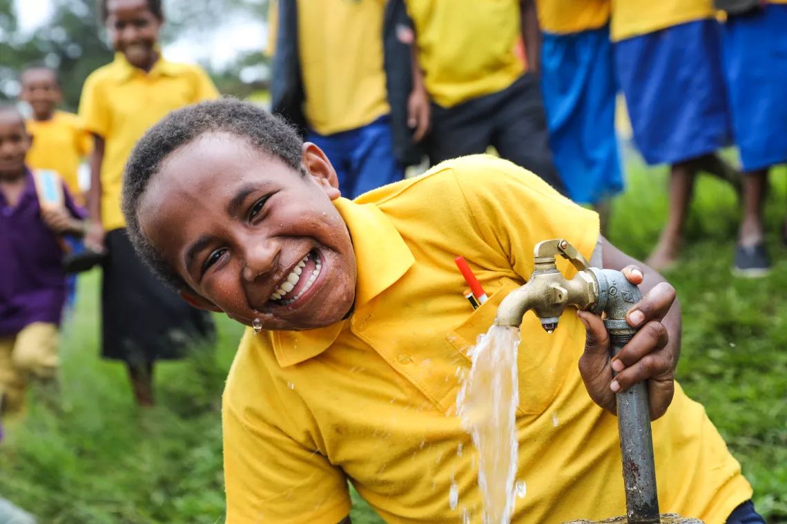 Un niño en papua Nueva Guniea sonríe mientras agua sale de un grifo