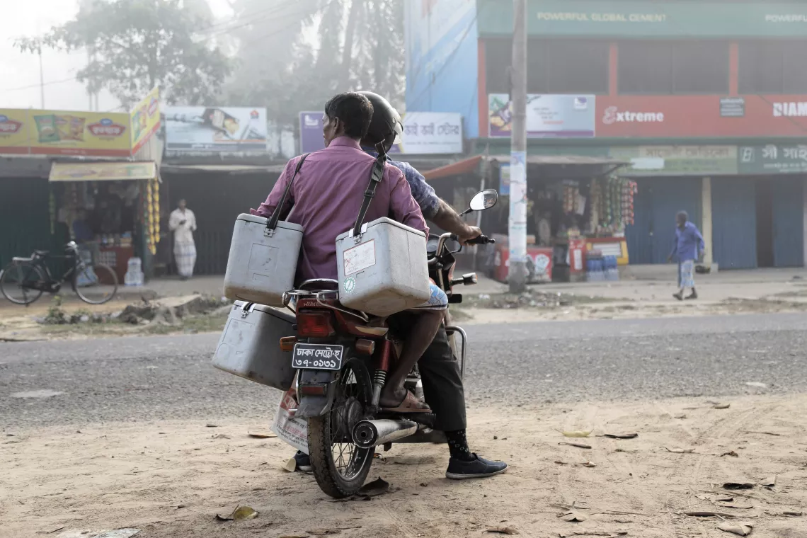A man holding coolers rides on the back of a motorbike, Bangladesh