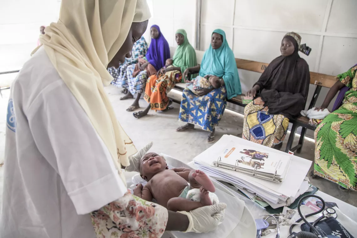 A midwife weights a newborn at a health centre, Nigeria