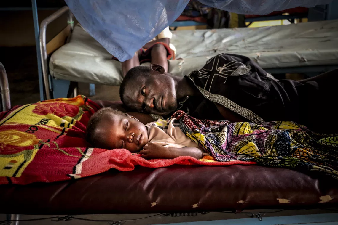 Central African Republic. A man lays with his child at a clinic.