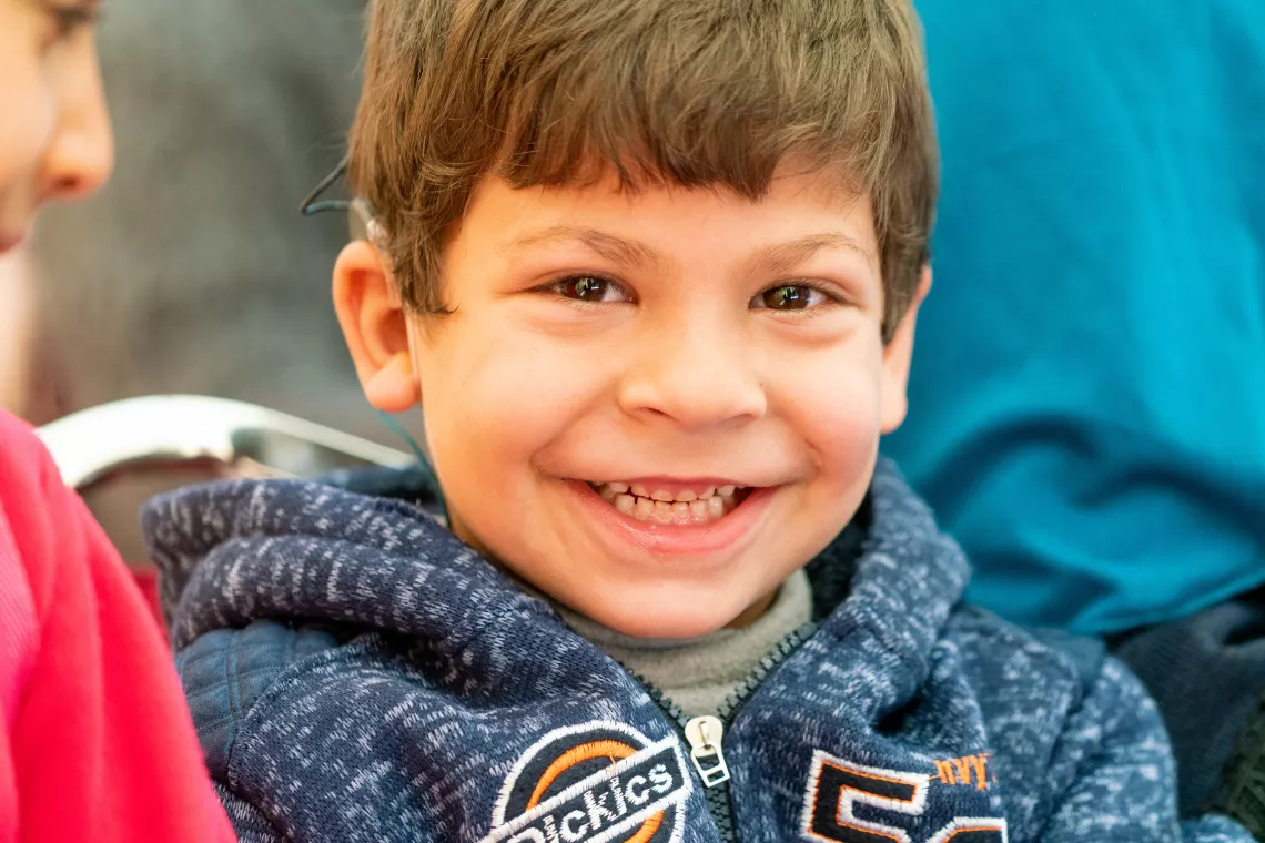 A young boy wearing an assistive device listens to a speaker at an awareness-raising session.