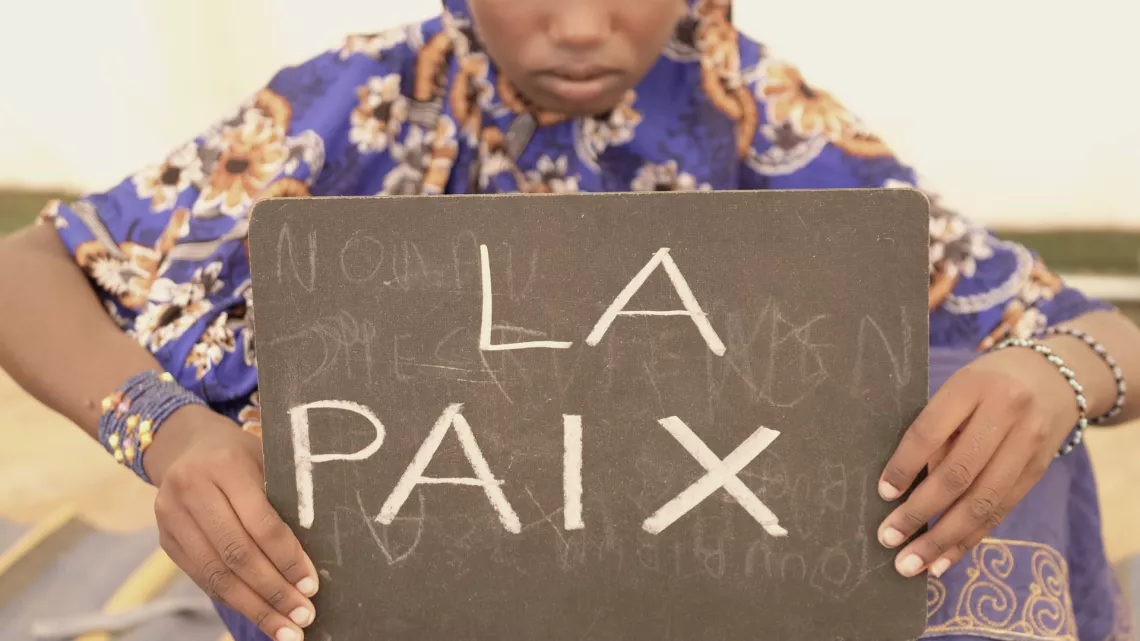 Mali. A girl holds a slate bearing the word "Peace".