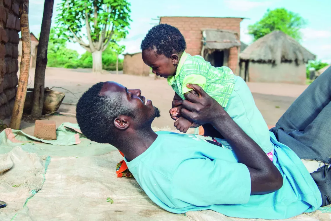 Lukas plays with his daughter beside their home in Kholowa, Zambia. 
