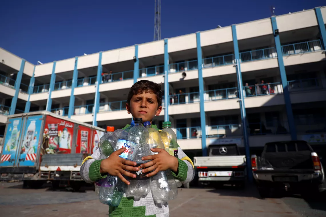 Gaza. A boy holds empty water bottles as he looks for clean water.