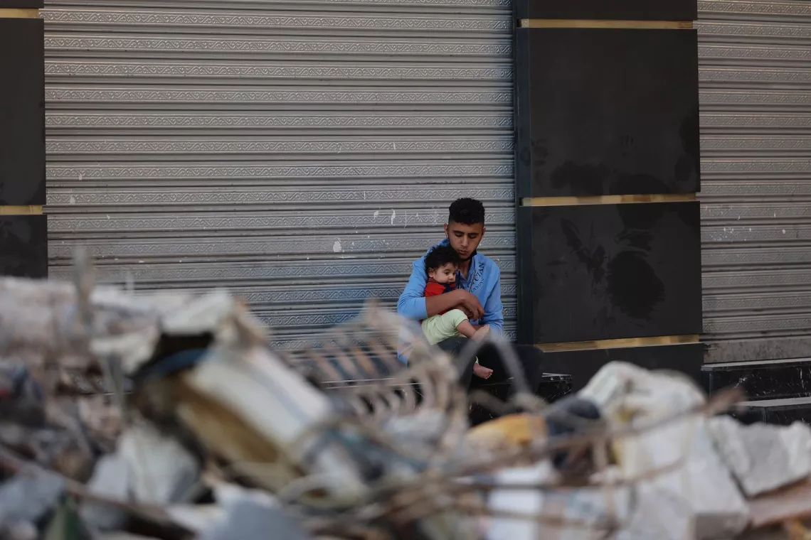 Gaza. A man holds his son outside a store near their damaged home.