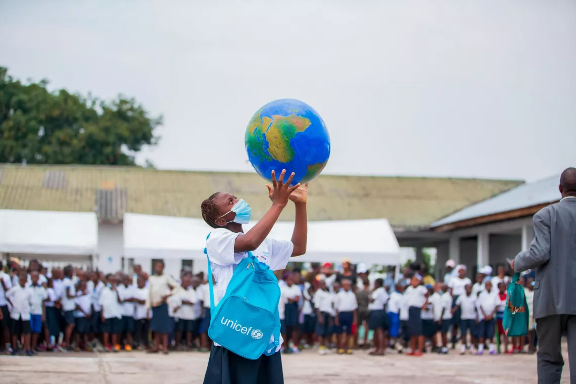 A young woman outside her school in the Democratic Republic of the Congo holds an inflatable globe in the air.