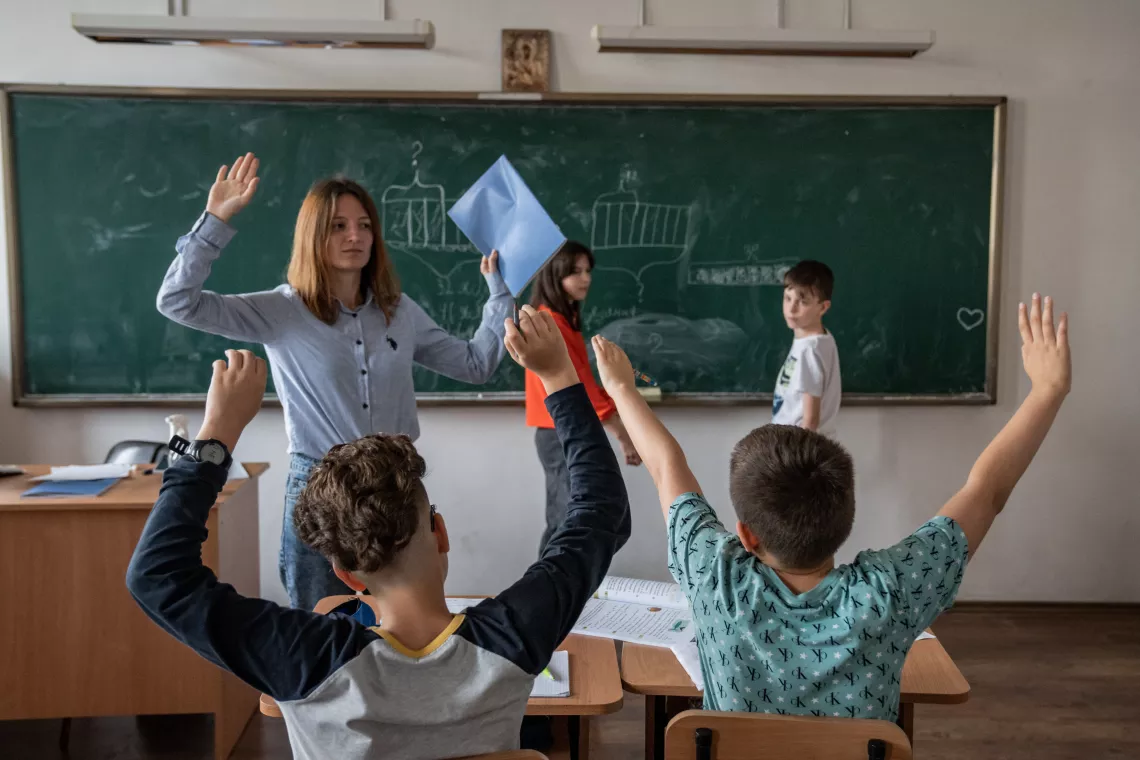 Romania. A teacher holds her arms up in the air in a classroom.