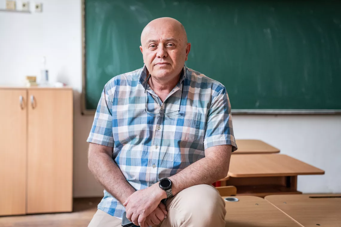 Romania. A teacher sits on a desk in a classroom.