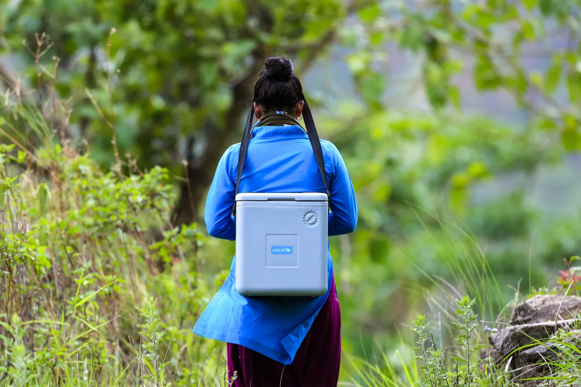 A health worker with a vaccine carrier on her back en-route to a community outreach session to vaccinate children under the routine vaccination programme.