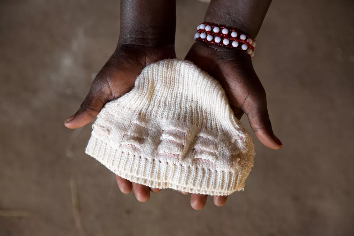 Uganda. A woman holds up a hat that belonged to her late son.