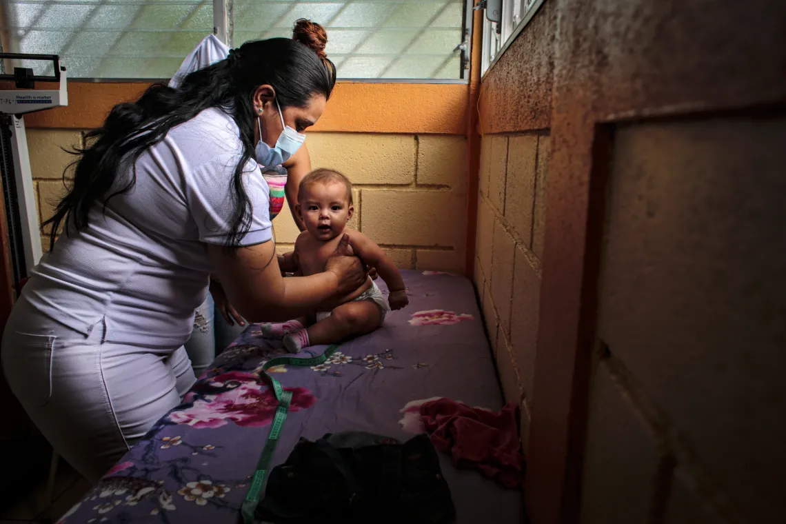 A female nurse listens to the heartbeat of an infant.