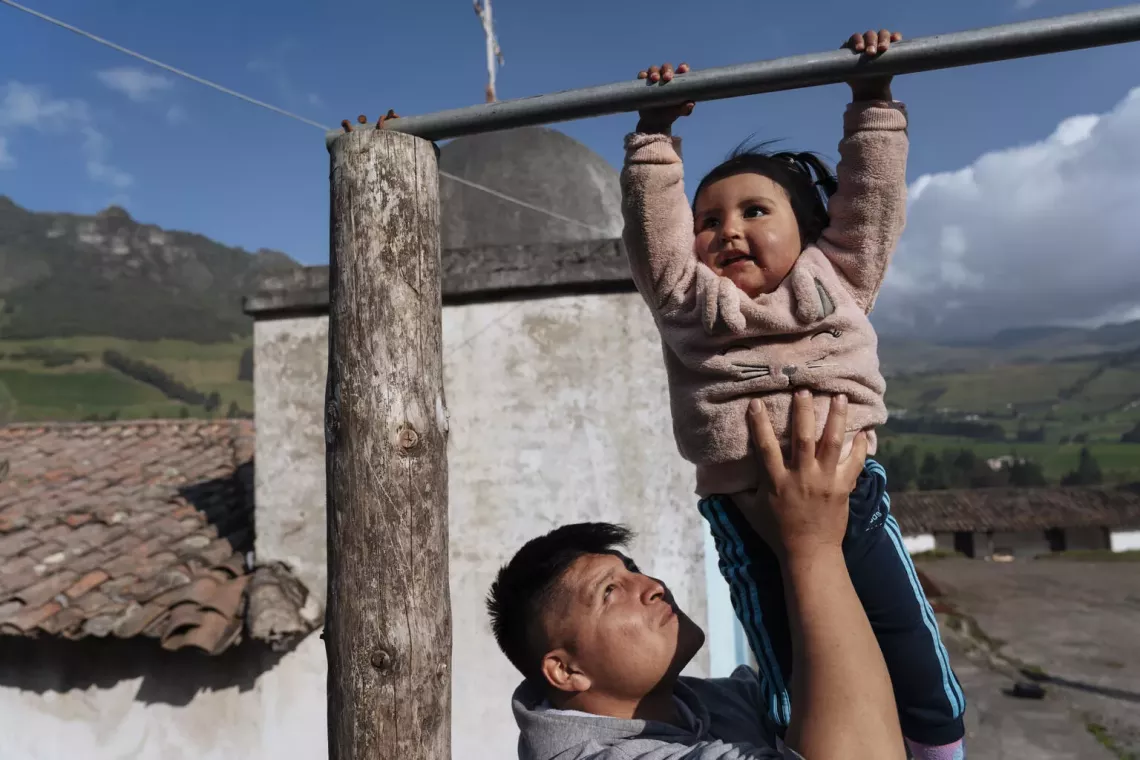 Richard holds his two-year-old daughter, Aysel, as she swings on a pole outside their home in Turugucho, Ecuador. 