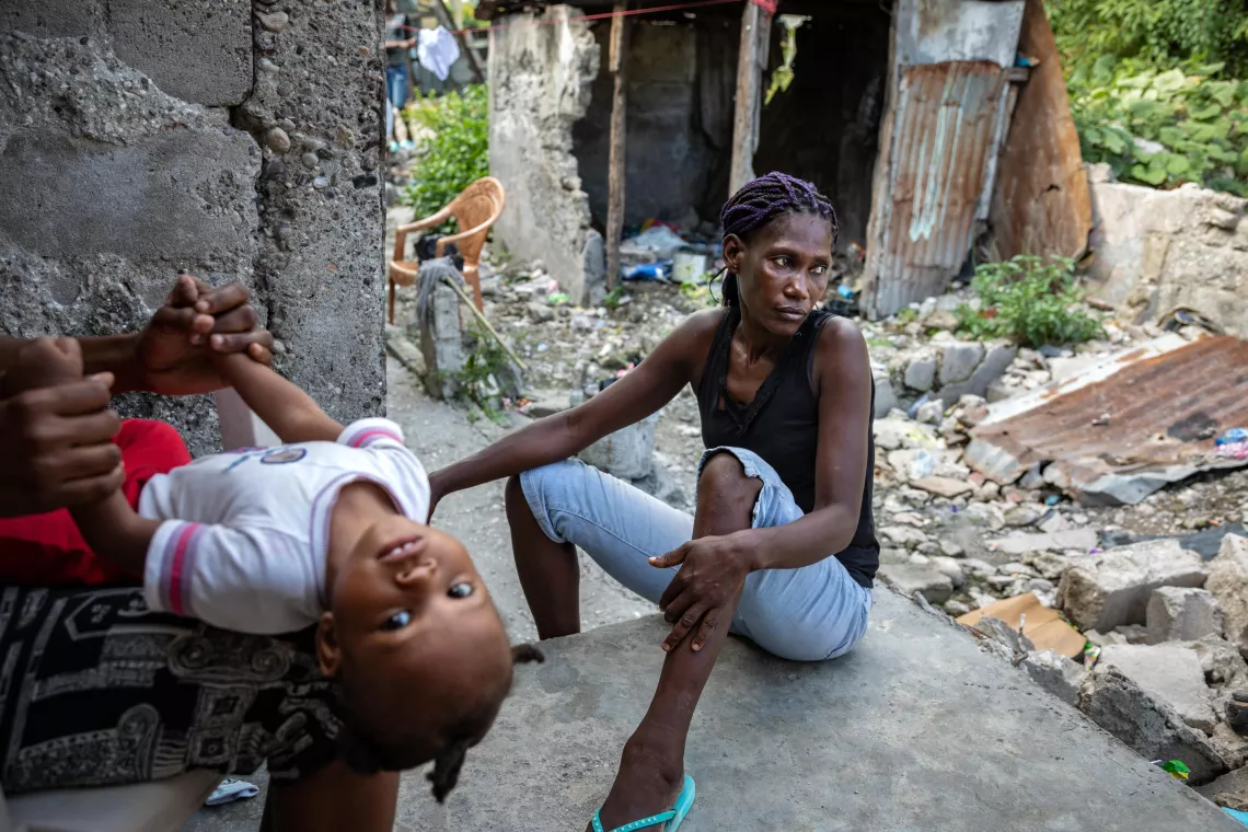 On 18 July 2022, a neighbour plays with baby Valentine on the stoop of Yolande Felix's home in Les Cayes, Haiti. 