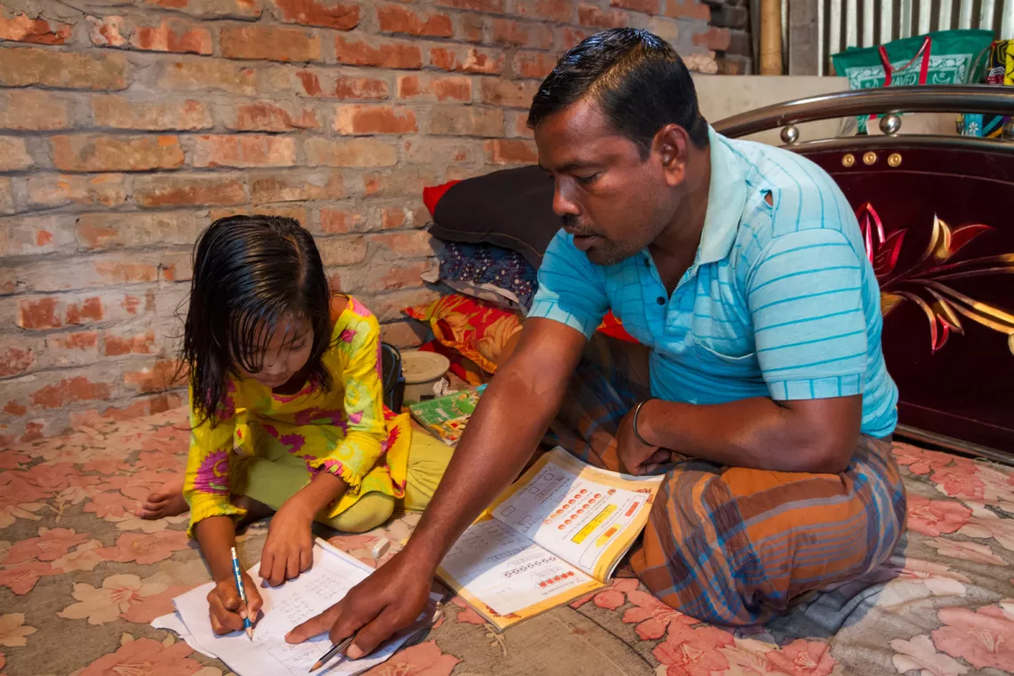 在孟加拉国达卡米尔布尔的Duaripara贫民窟，45岁的阿扎鲁·伊斯兰（Azharul Islam）在辅导7岁的女儿阿杜瑞（Aduri）写作业。他和妻子打算供他们的女儿们上学到至少18岁。