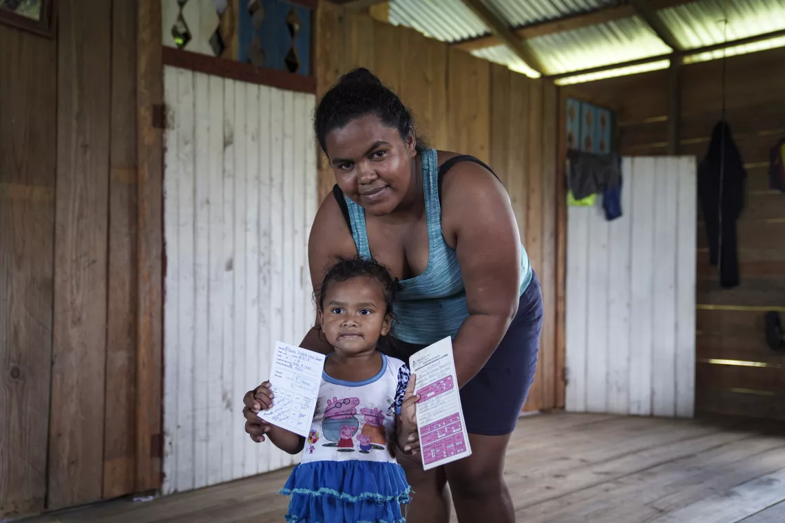 Florencia Mena stands with her 3-year-old daughter, Rihana, who holds her vaccination cards to show them to the health personnel.
