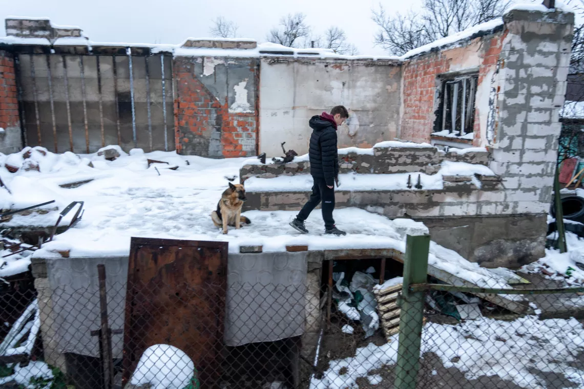 Ukraine. A boy walks with his dog in the snow around the remains of his family home in Irpin.