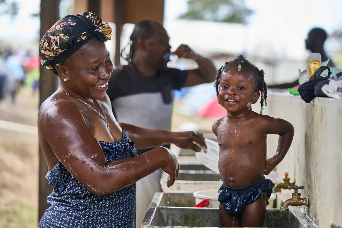A smiling little girl is getting washed by her mother in a big sink.