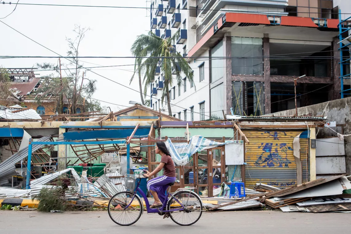 Una mujer pasa en bicicleta junto a edificios que sufrieron graves da&ntilde;os durante el cicl&oacute;n Mocha en el estado de Rak&aacute;in, en Myanmar, el 14 de mayo de 2023.
