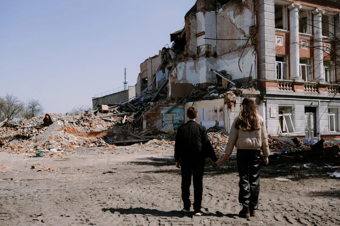 Ukraine. Siblings Anastasia and Mykhailo stand in front of a destroyed school in Eskhar.