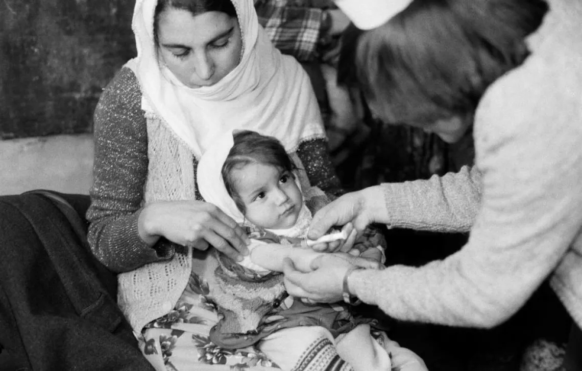 A girl is vaccinated while sitting in her mother's lap.