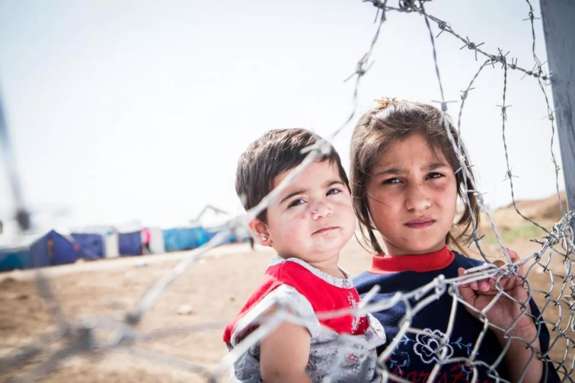 A boy and a girl look through a fence. Iraq, 2013.
