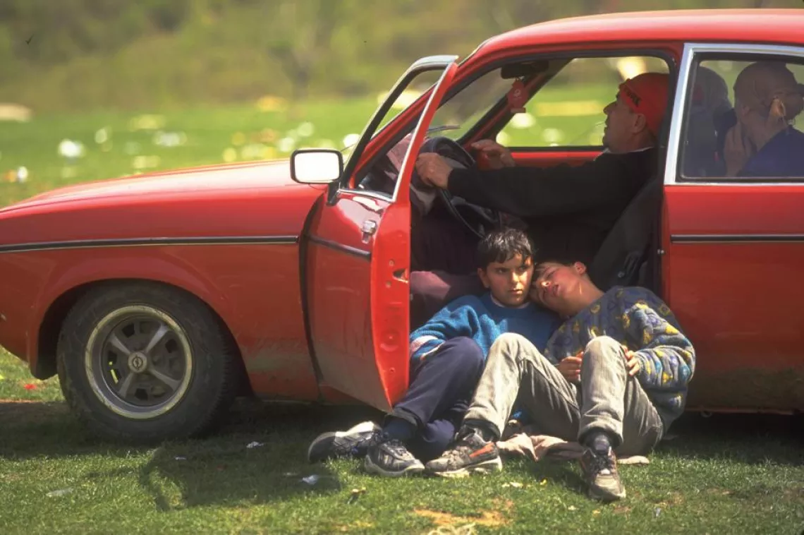 Refugees rest inside and outside a red car.